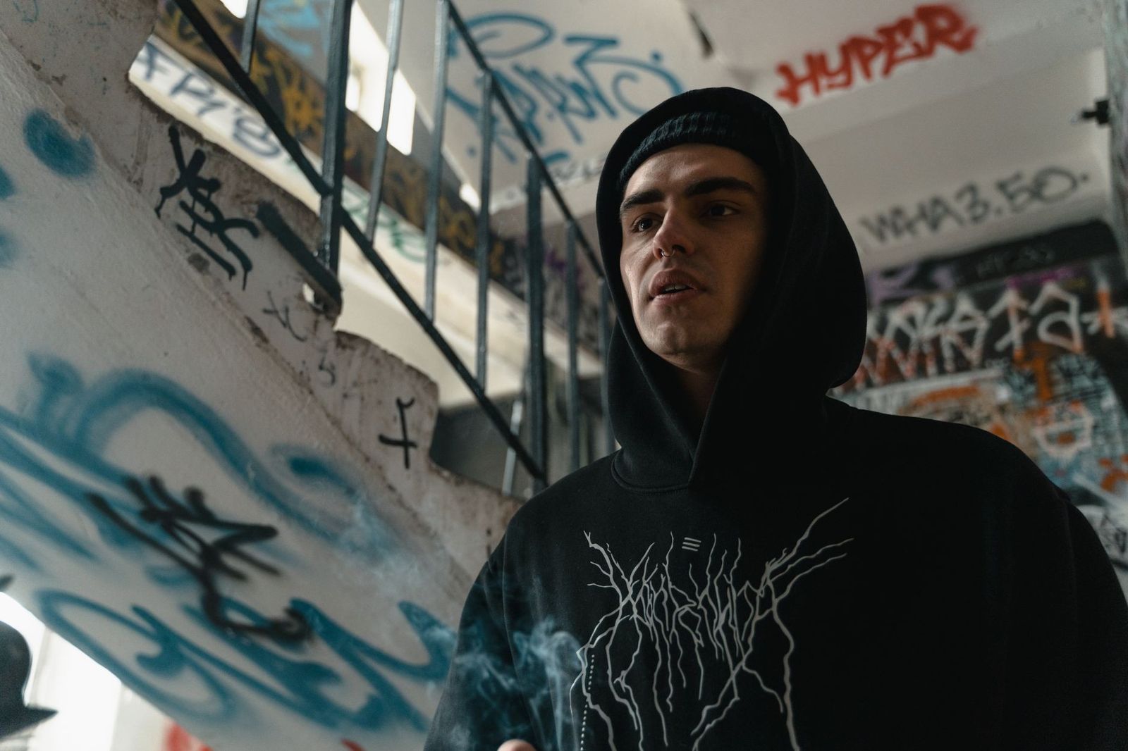 Person wearing a black hoodie stands by graffiti-covered stairs